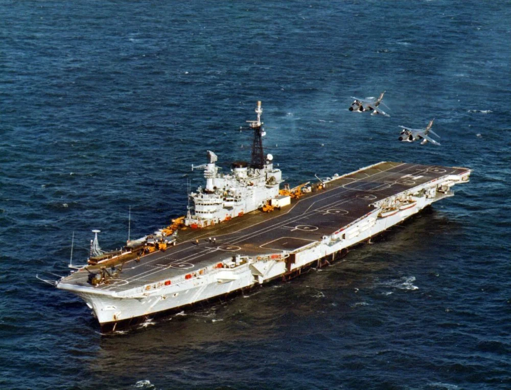 HMS Hermes (R12) overflown by RN Sea Harrier FRS.1 of 700 Sqn (c1980).webp