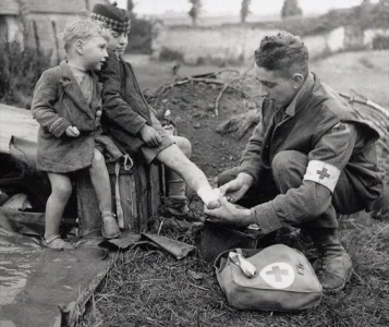 A medic bandages the injured foot of a child while his younger brother looks on, 1944.webp