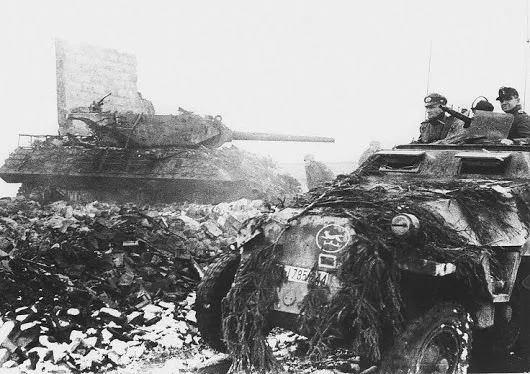 A German half-track passes a knocked out American M10 tank destroyer during the Battle of the Bulge